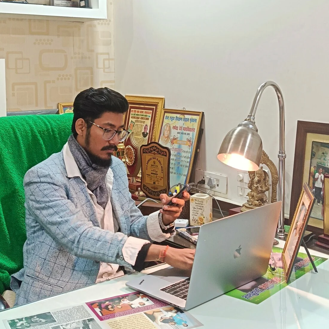 Aman today at his office desk with awards behind him